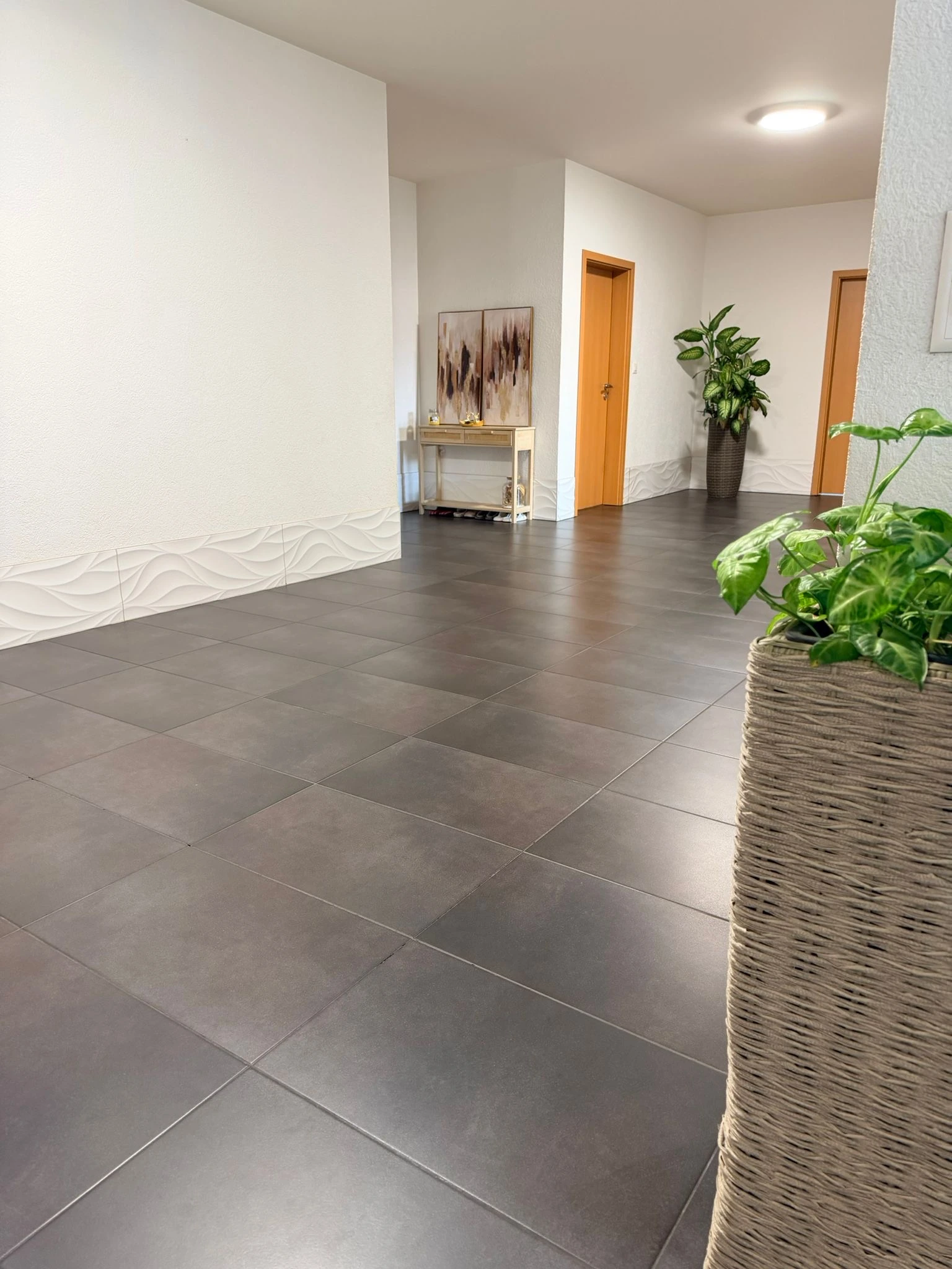 Carrelage gris du couloir vu en biais, avec faïence blanche à relief ondulé le long des murs et des retours d’angle