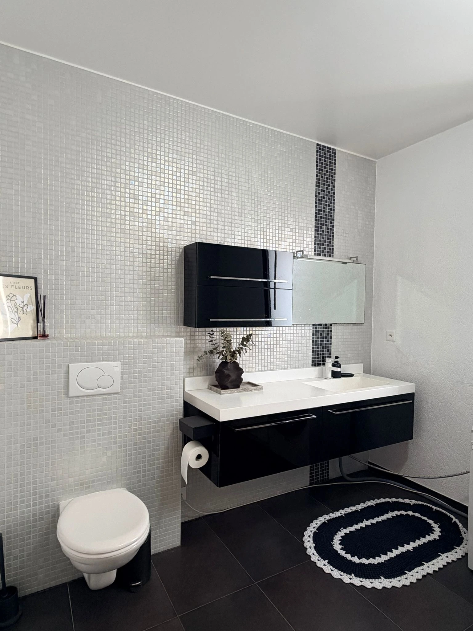 Lavabo et WC devant une mosaïque claire à bande foncée, avec carrelage gris foncé au sol