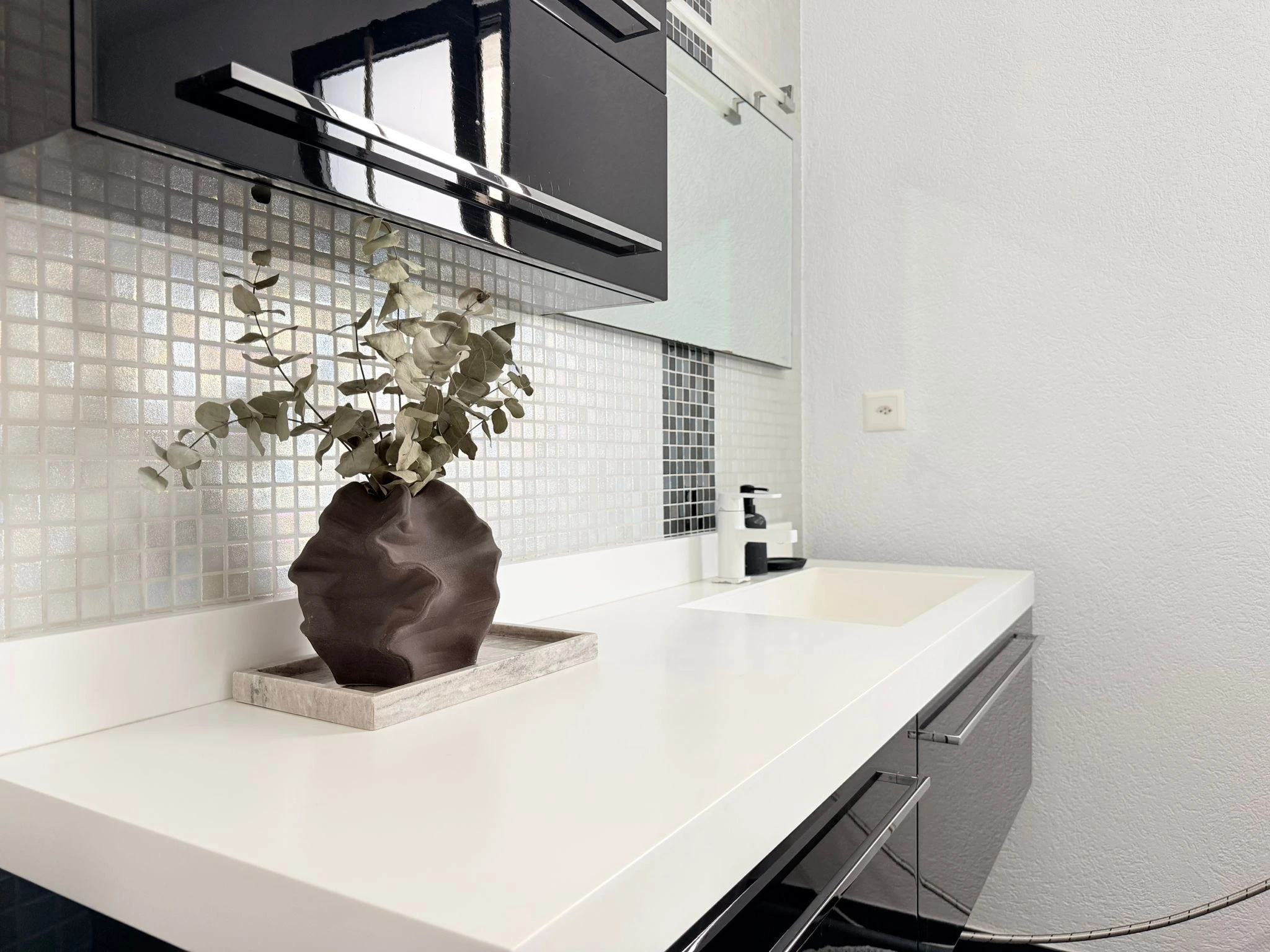 Lavabo blanc vu en perspective devant une mosaïque claire aux reflets irisés et une bande de mosaïque foncée