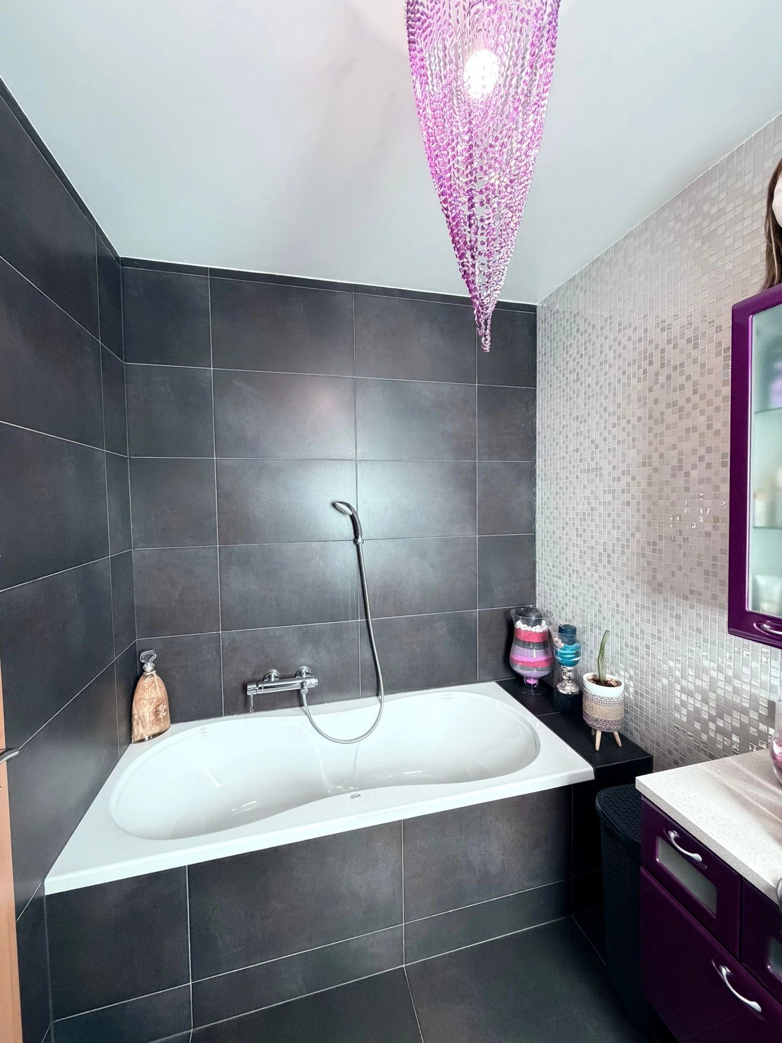 Baignoire habillée de carrelage gris anthracite, avec faïence assortie et mosaïque claire sur le mur adjacent