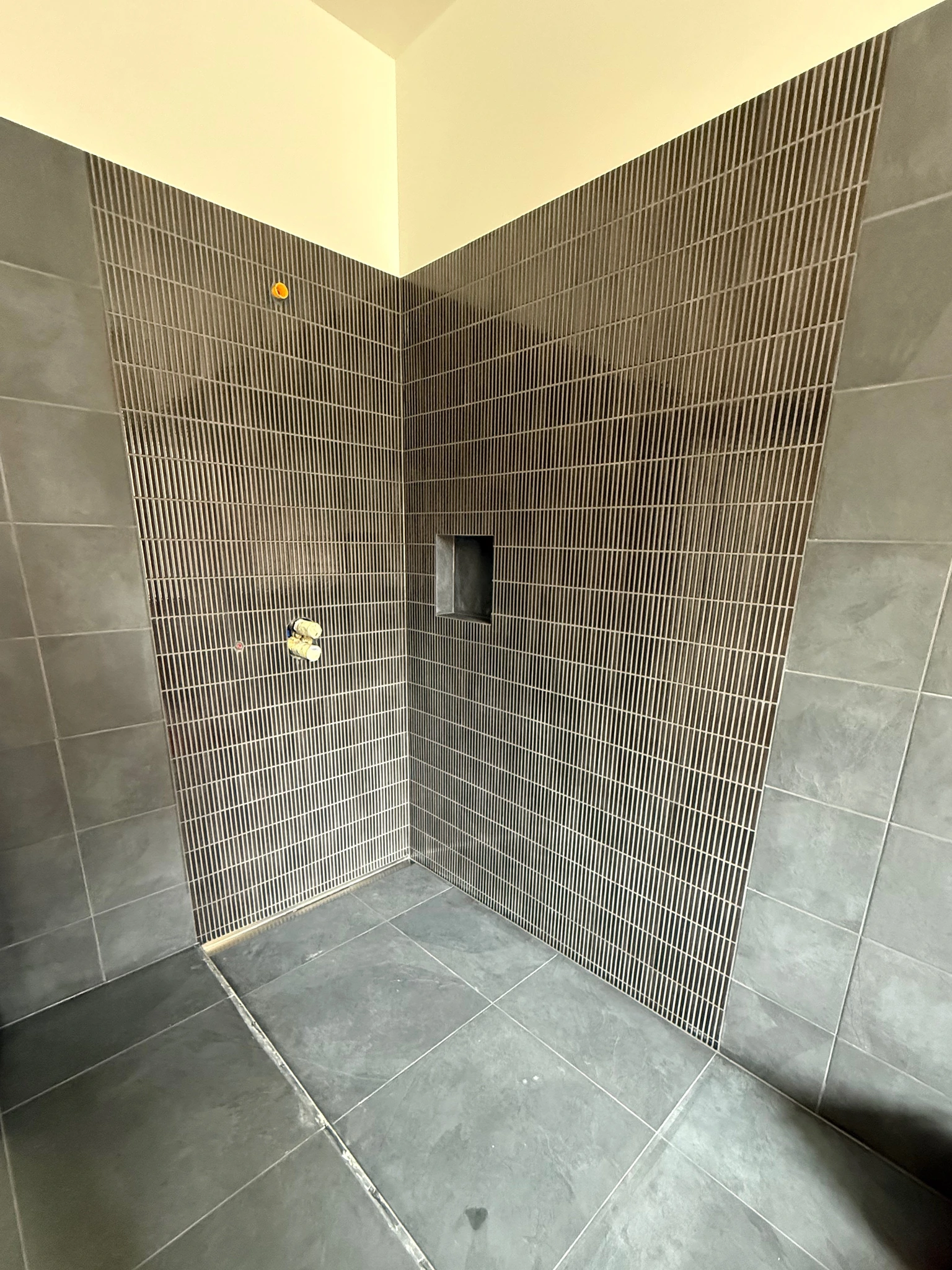 Douche côté couloir avec carrelage gris, faïence décorative verticale et niche intégrée