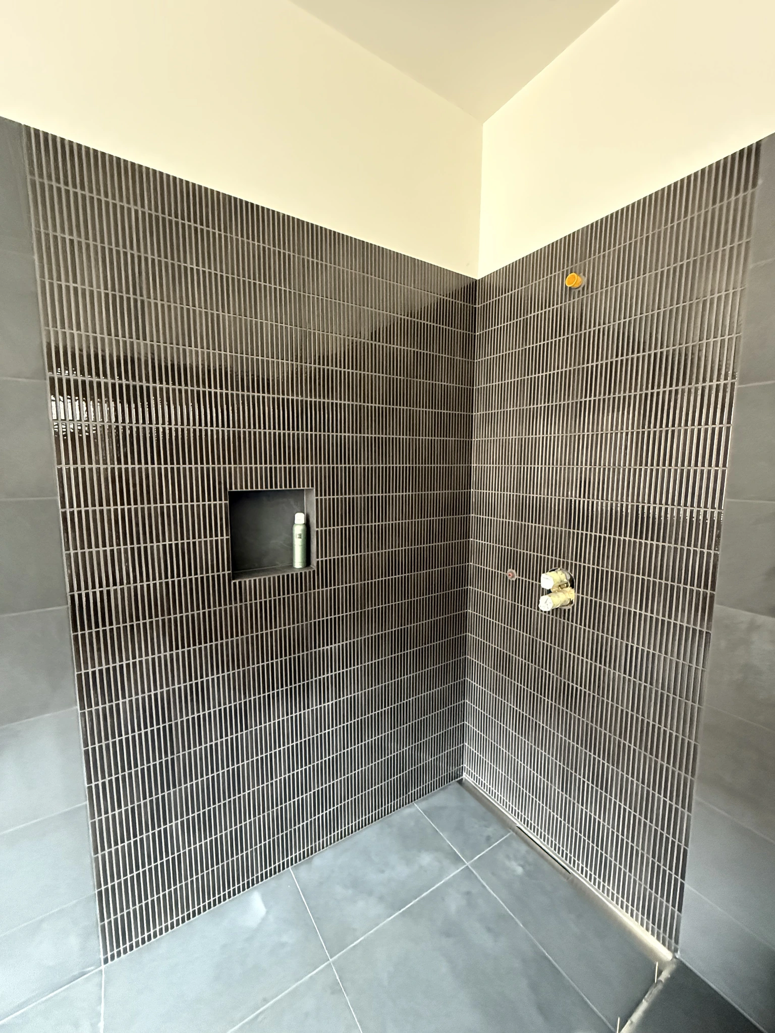 Douche de la chambre parentale avec faïence décorative verticale, niche intégrée et sol carrelé gris