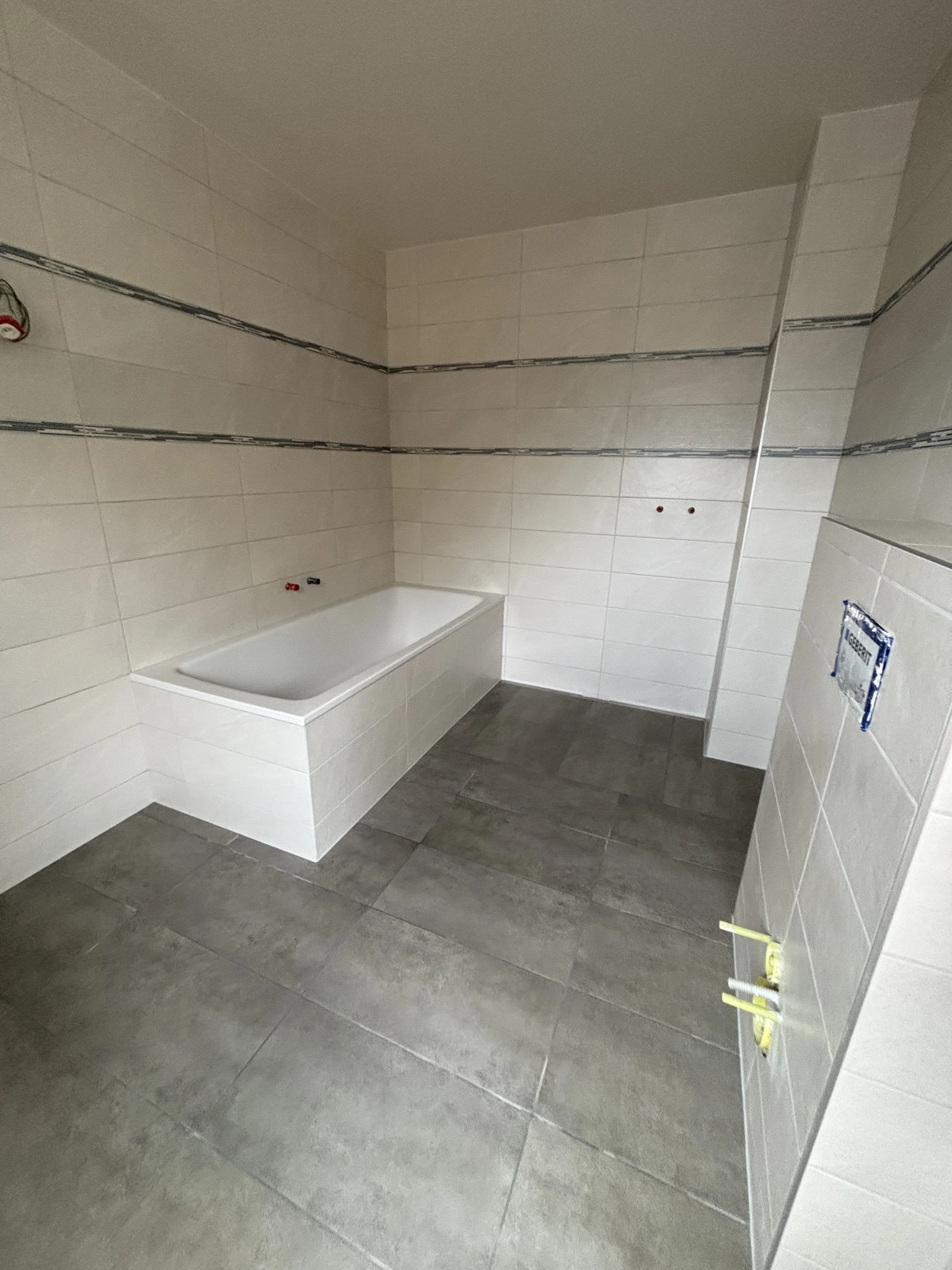 Vue d’ensemble de la salle de bains avec baignoire habillée de faïence claire, deux frises décoratives et carrelage gris au sol