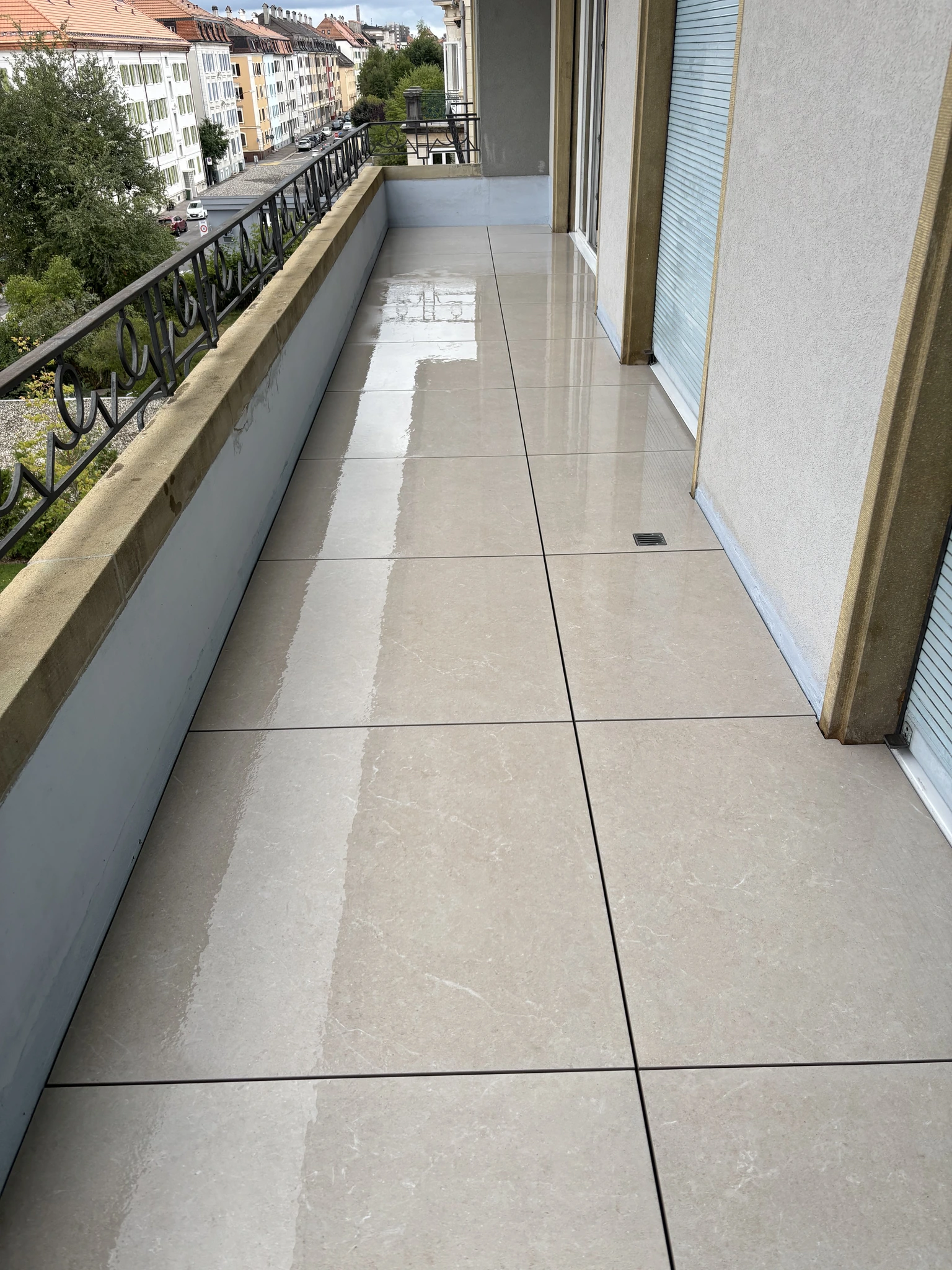 Balcon terminé avec dalles grand format beige clair posées sur plots et découpes autour de l’évacuation